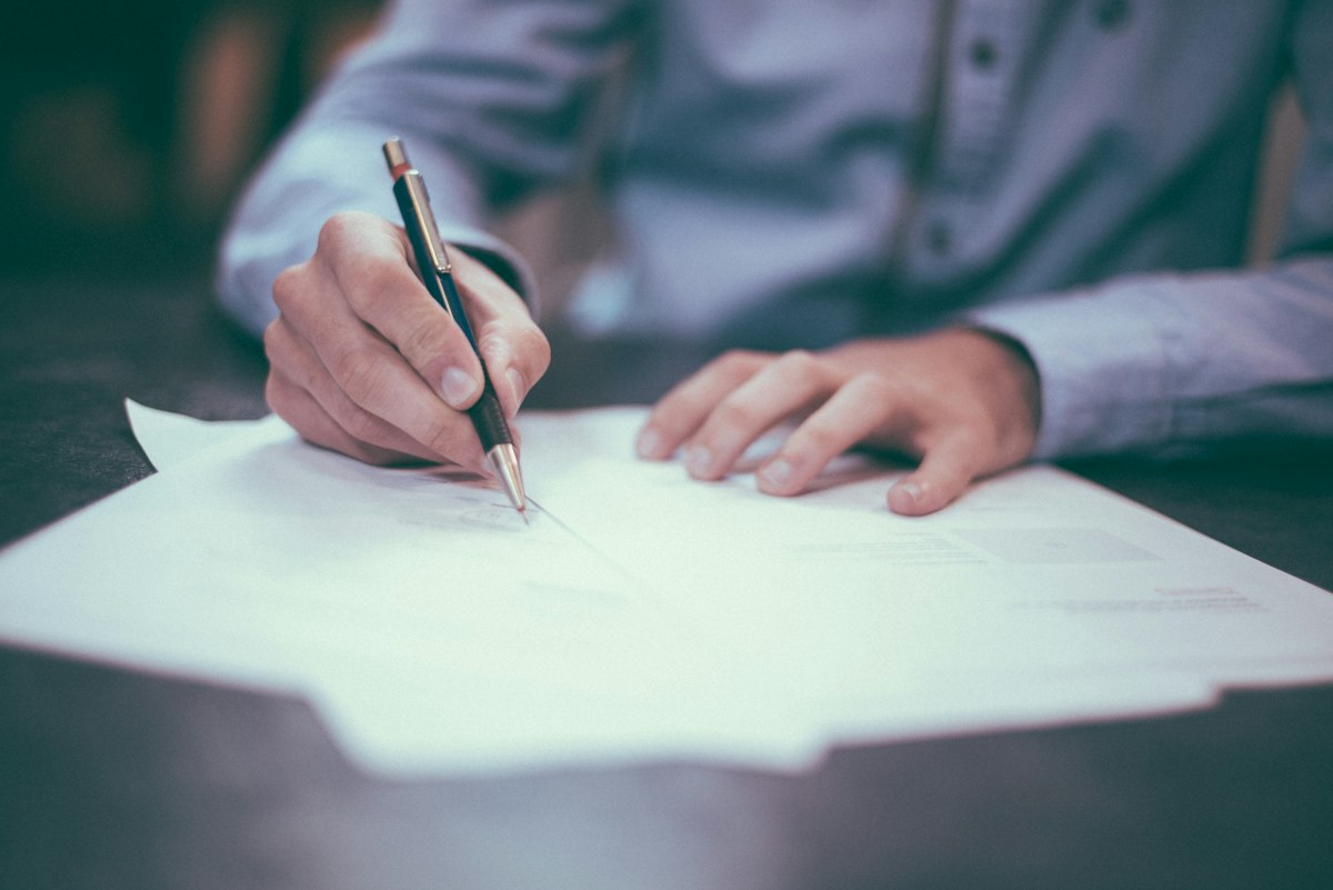 Hand holding a pen over a signed agreement